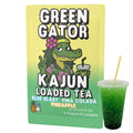 Image of the single Green Gator packet (with the Hawaiian-themed alligator) placed next to a clear cup of the prepared, intensely green-colored loaded tea.